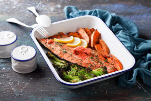 Baked sockeye salmon fish fillet with roasted sweet potato and broccoli, in enameled baking dish, selective focus